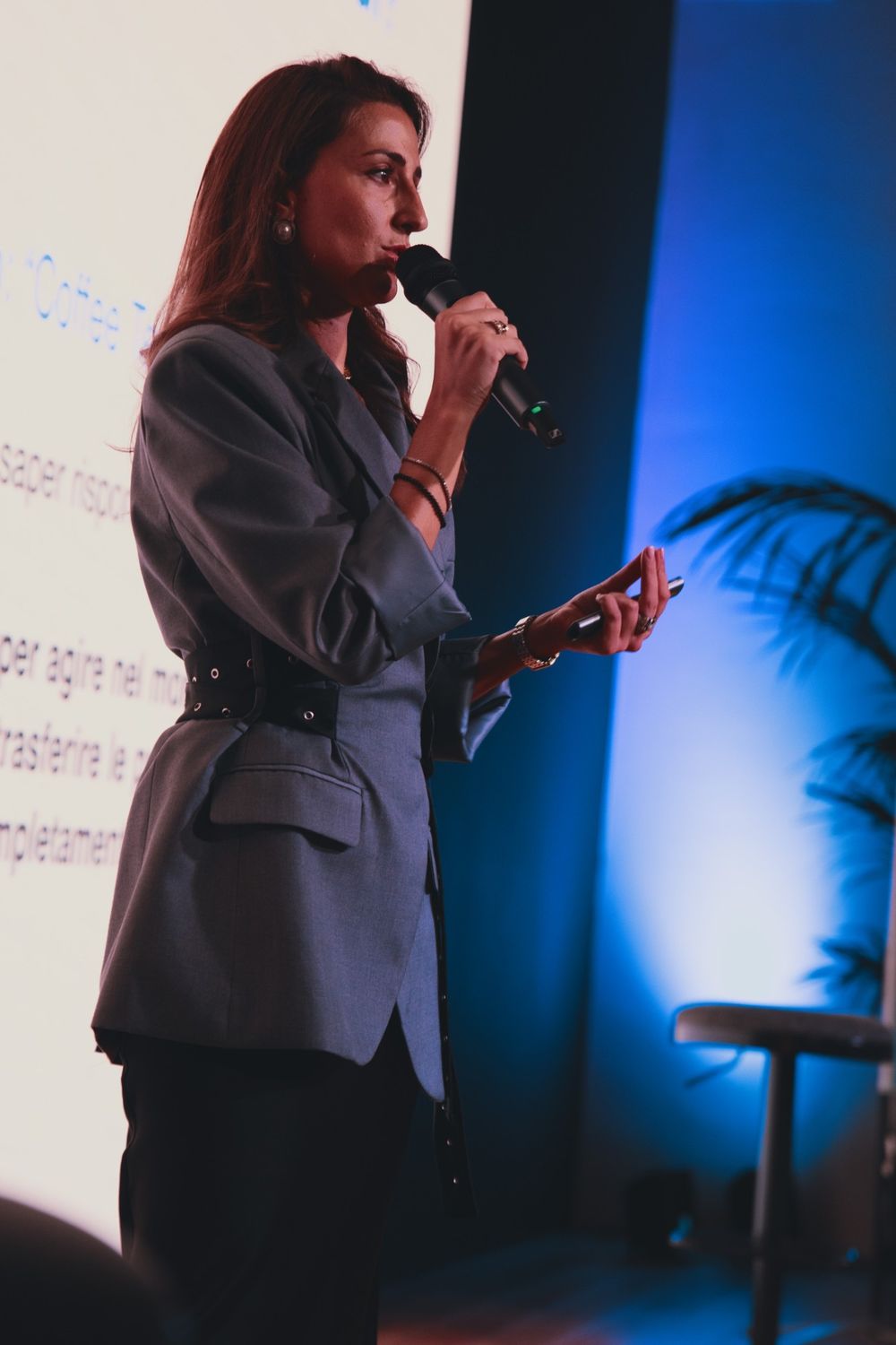 Camilla Brossa di profilo al microfono, in luce blu, accanto alle slide del suo intervento